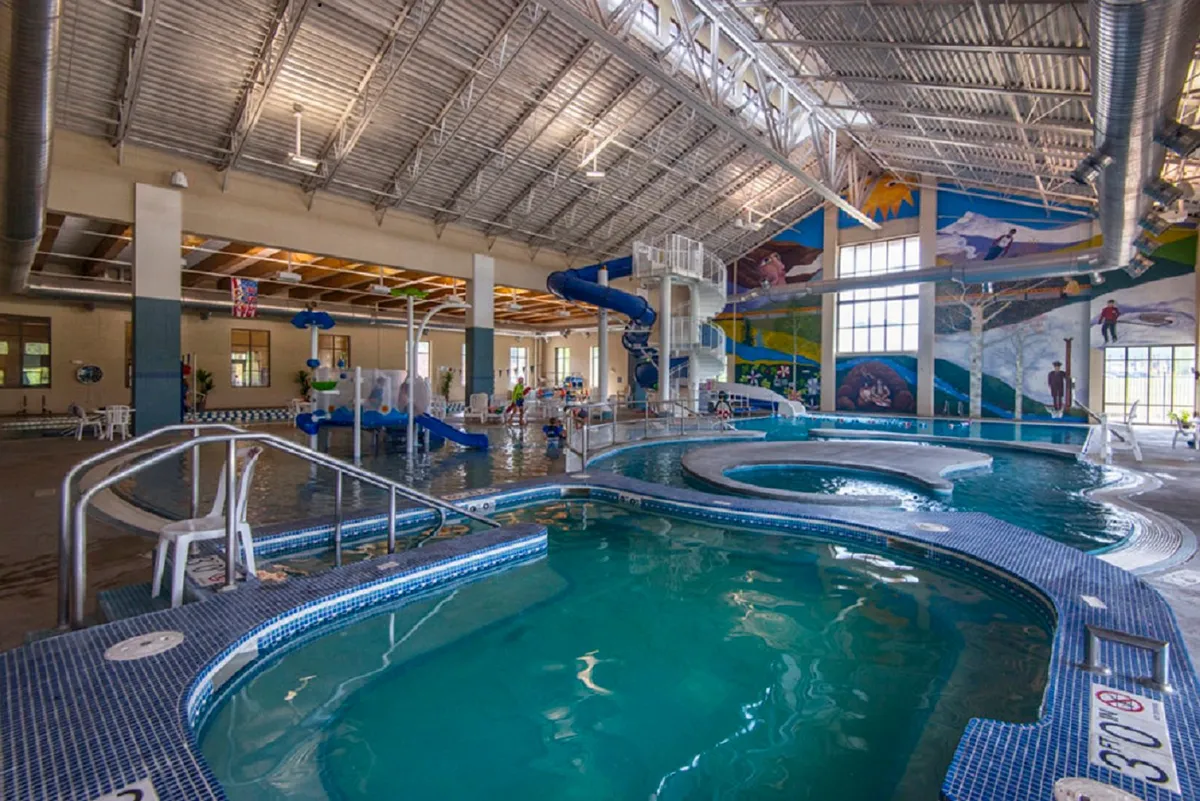 An indoor recreation center scene filled with colorful water slides, swimming pools, playful murals, and ample seating. The space is lively and designed for family fun and group activities.