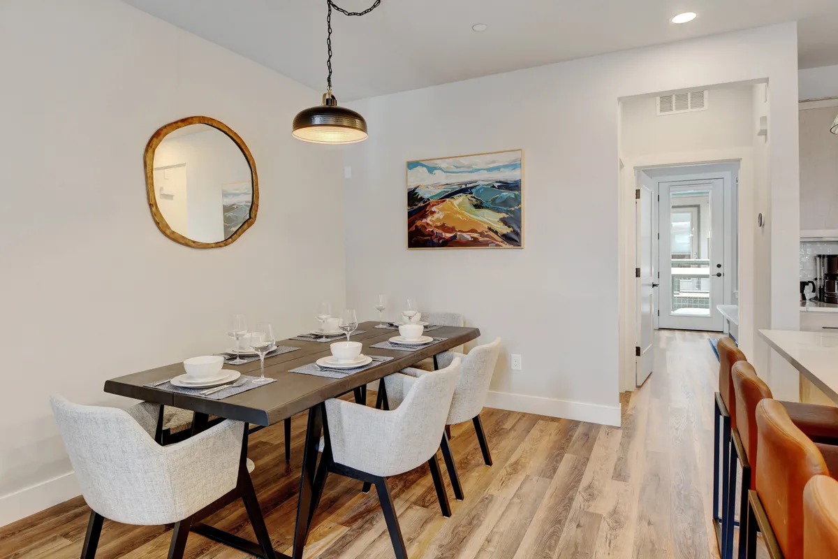 A stylish dining area with a wooden table set for a meal, complemented by contemporary wall art and a mirror. The space is designed for socializing, hearty meals, and shared moments with family or friends.