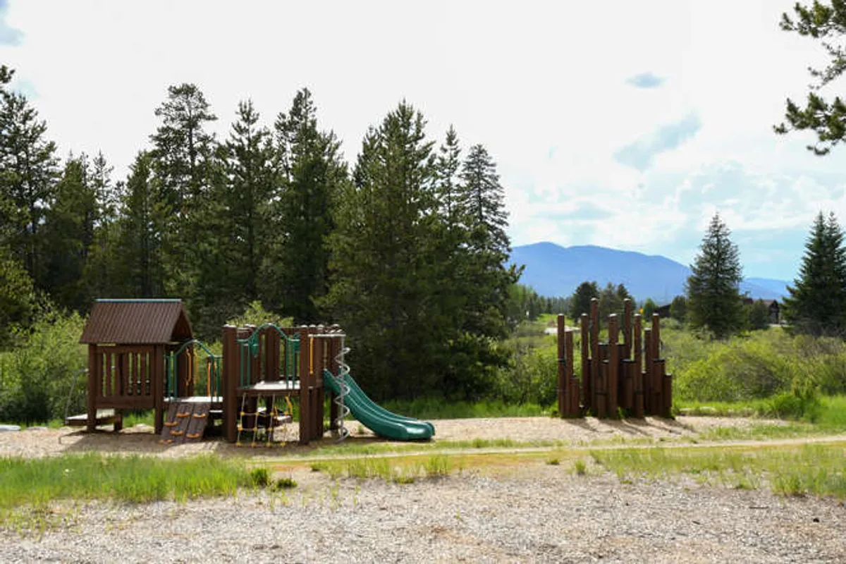 An outdoor playground structure surrounded by trees, featuring slides and climbing apparatus. Children can be seen playing, evoking a sense of joy and family fun in a natural setting.