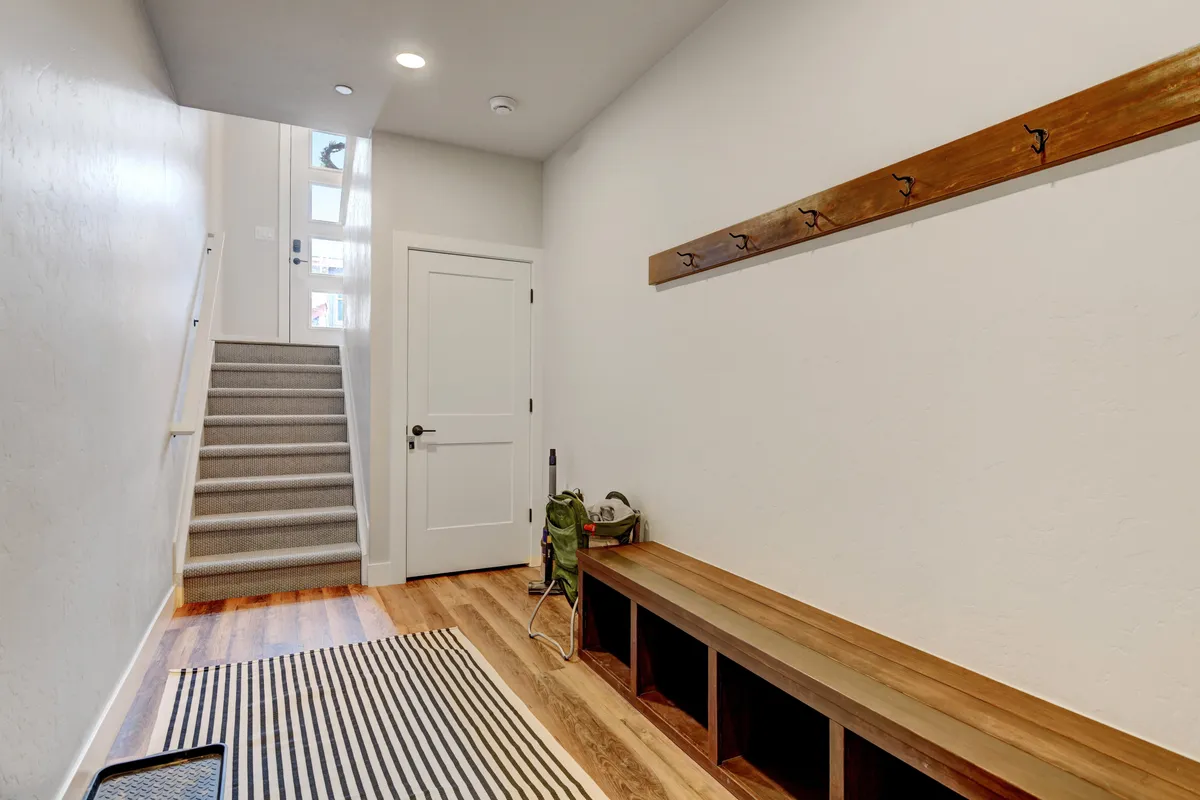 An inviting entryway with a wooden bench, coatrack, and staircase. The space is tidy and functional, ideal for taking off boots, hanging coats, and unloading after outdoor activities.