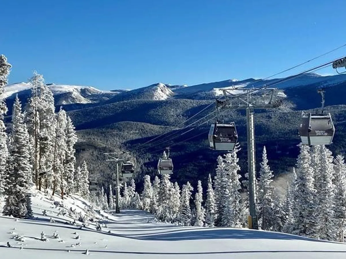 A stunning exterior shot of ski lift gondolas gliding above snow-covered trees with a dramatic mountain range in the background. The image radiates excitement and accessibility to mountain sports like skiing, snowboarding, and hiking.