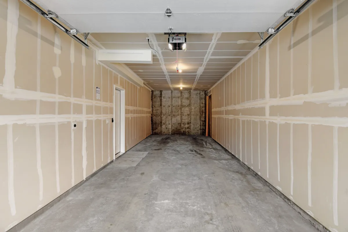 This image displays a functional garage space with visible exposed walls, a concrete floor, and a garage door opener. The area is uncluttered, clearly emphasizing both the potential for parking and ample storage for gear or bikes.